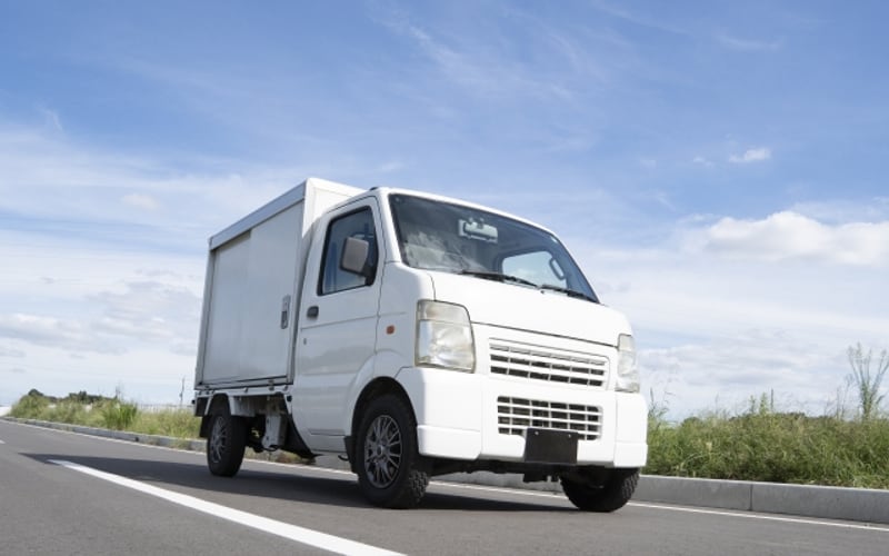青空の下、道路を走る白い軽貨物トラック